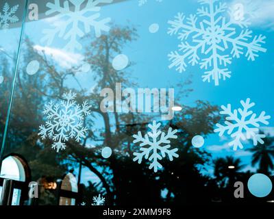 Joyeux Noël et bonne année concept. Beaucoup de décoration d'autocollant de flocon de neige de Noël sur verre de fenêtre dans un café avec fond de ciel bleu et arbres, re Banque D'Images