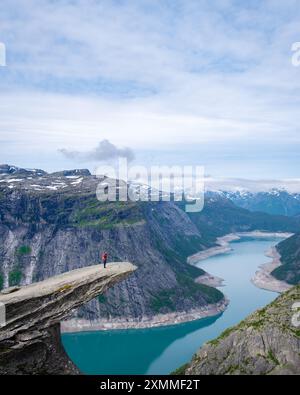 Un randonneur se dresse au bord de la falaise de Trolltunga en Norvège, surplombant un vaste et pittoresque fjord. Femmes asiatiques randonnant la Trolltunga, Norvège Banque D'Images