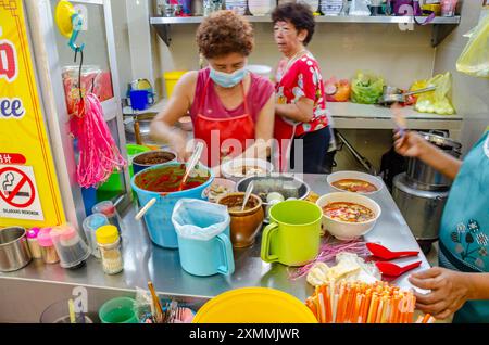 Une dame prépare une commande de nourriture à un étal dans la cour de restauration du marché Tanjung Bungah à Penang, en Malaisie Banque D'Images