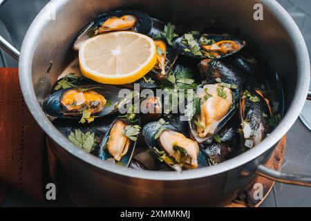 Moules au vin blanc avec persil et citron dans une casserole sur une table grise. Gros plan. Cuisine méditerranéenne, recette française traditionnelle. Haute qualité p Banque D'Images