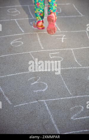 Houssette dessinée à la craie sur le trottoir. Pieds d'enfant. Jambe de fille sautant sur des places dans la rue. Banque D'Images