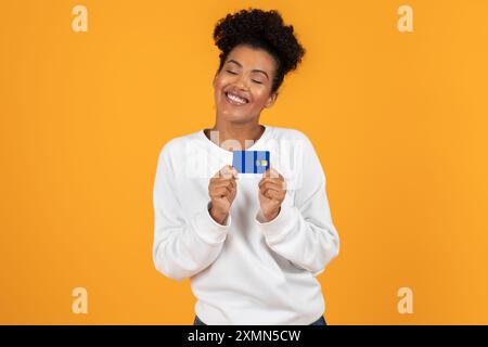 Femme souriante tenant la carte de crédit sur fond jaune Banque D'Images