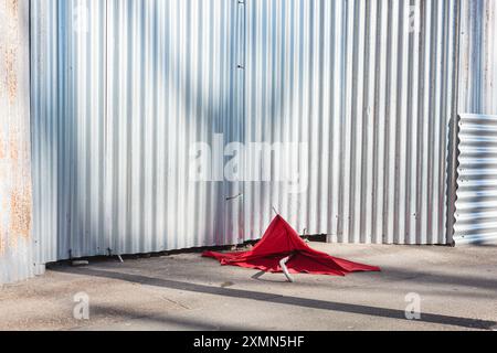 Parasol rouge cassé sur le sol dans une rue de la ville, avec un fond à volets Banque D'Images