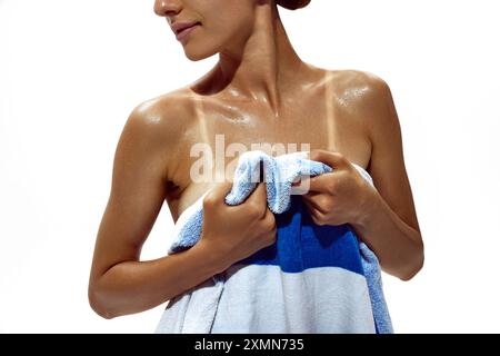 Femme s'enveloppe dans une serviette, révélant des lignes de bronzage sur sa peau profondément bronzée sur fond blanc de studio. Banque D'Images