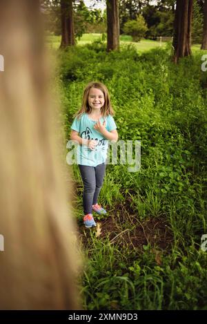 Petite fille heureuse se cachant derrière l'arbre dans la forêt Banque D'Images