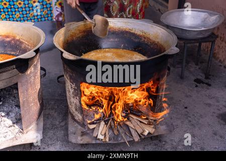 Une personne fait cuire des aliments dans une grande casserole au-dessus d'un feu Banque D'Images