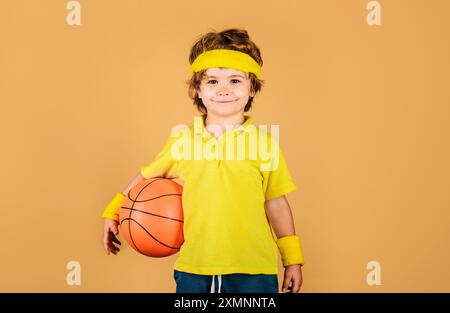 Petit joueur de basket-ball en t-shirt jaune avec ballon de basket-ball. Garçon souriant en vêtements de sport avec basket-ball. Sport pour les enfants, mode de vie sain et Banque D'Images