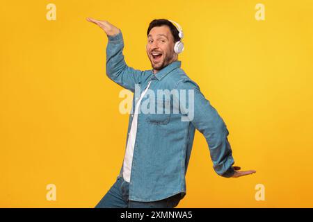 Homme heureux dansant sur fond jaune tout en portant des écouteurs Banque D'Images