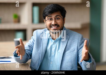 Homme souriant faisant des gestes lorsqu'il est assis au bureau dans le bureau Banque D'Images