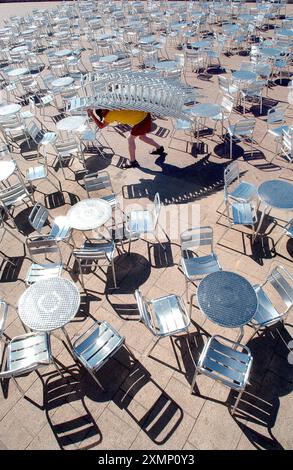 Photo de Roger Bamber : 13 juin 2003: le barman Sean Gourley transporte une pile de 16 chaises sur la terrasse en face du Gemini Lounge et du Beach Bar sur la promenade inférieure de Brighton front de mer afin de se préparer aux foules de vacanciers assoiffés affluant à la plage le jour le plus chaud de l'année. Banque D'Images