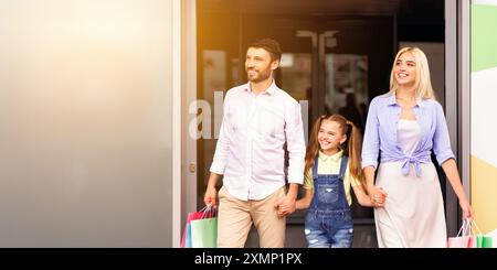 Happy Family quittant le magasin avec des sacs à provisions le jour ensoleillé Banque D'Images