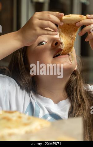 Jolie fille et pizza aux quatre fromages gros plan. Une jeune fille pré-adolescente regarde dans le cadre alors qu'elle se prépare à manger de la pizza. Photo verticale. Foyer sélectionné. Qual. Élevé Banque D'Images