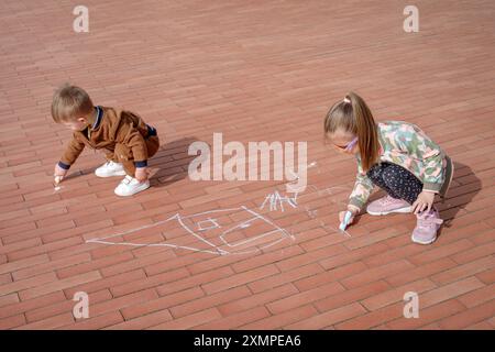 Fille avec son frère cadet griffonnant avec de la craie sur le trottoir, vue de dessus Banque D'Images