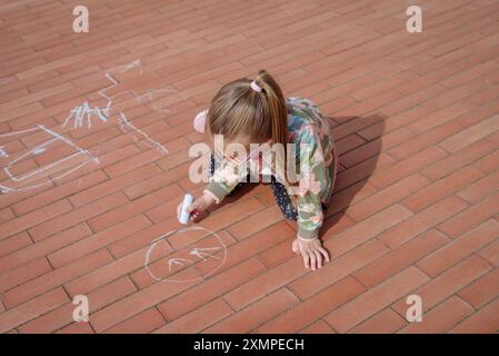 Petite fille griffonnant avec de la craie sur le trottoir, vue de dessus Banque D'Images