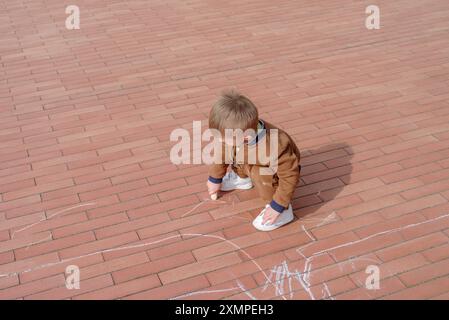 Petit garçon griffonnant avec de la craie sur le trottoir, vue de dessus Banque D'Images