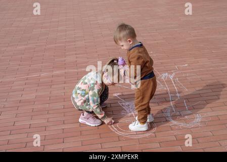 Fille avec son frère cadet griffonnant avec de la craie sur le trottoir, vue de dessus Banque D'Images