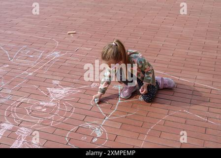 Petite fille griffonnant avec de la craie sur le trottoir, vue de dessus Banque D'Images