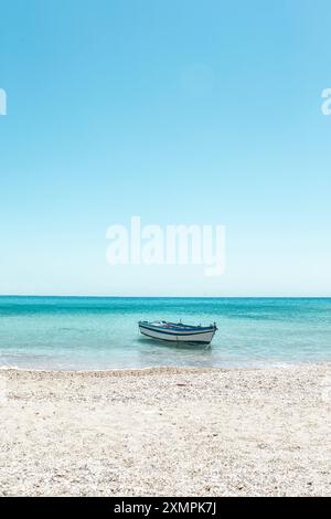 Un petit bateau repose doucement sur les eaux calmes de Donousa, entouré par la plage de sable chaud et le ciel bleu serein. Banque D'Images