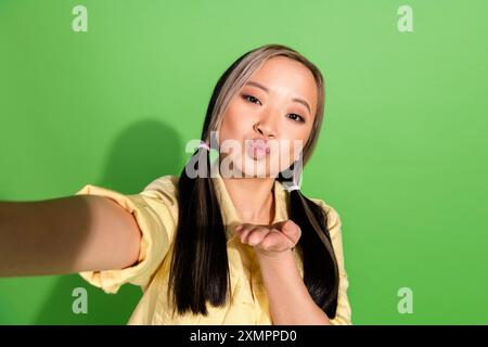 Portrait de jolie jeune femme prendre selfie envoyer air baiser vous portez veste isolé sur fond de couleur verte Banque D'Images