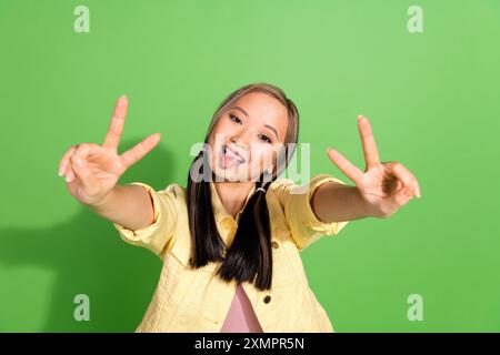 Portrait de jolie jeune femme montre v-sign Tongue wear veste isolée sur fond de couleur verte Banque D'Images