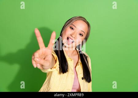 Portrait de jolie jeune femme v-sign languette out veste d'usure isolée sur fond de couleur verte Banque D'Images