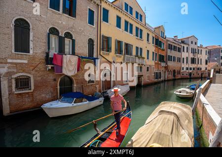 Venise, Italie - 05 juin 2024 : Gondolier en chemise à rayures rouges sur le canal de Venise. Banque D'Images