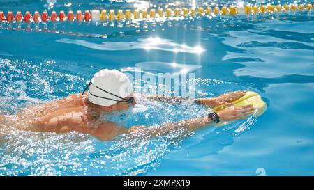 Photo vue de côté de l'homme concentré et stable, athlétique, nageur en casquette blanche et lunettes se propulse à travers la piscine à l'extérieur. Banque D'Images