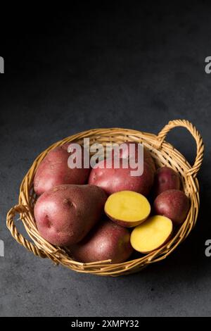 Belles pommes de terre nouvelles roses dans un panier en osier sur un fond sombre Banque D'Images