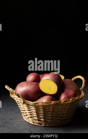 Belles pommes de terre nouvelles roses dans un panier en osier sur un fond sombre Banque D'Images