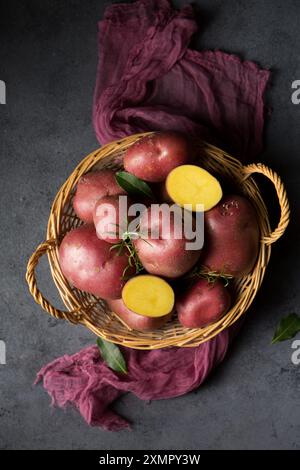 Belles pommes de terre nouvelles roses dans un panier en osier sur un fond sombre Banque D'Images