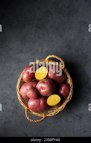 Belles pommes de terre nouvelles roses dans un panier en osier sur un fond sombre Banque D'Images