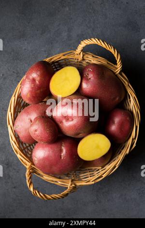 Belles pommes de terre nouvelles roses dans un panier en osier sur un fond sombre Banque D'Images