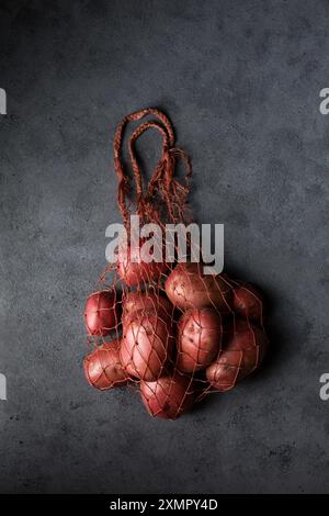 Belles pommes de terre nouvelles roses dans un sac en maille tricoté sur un fond sombre Banque D'Images