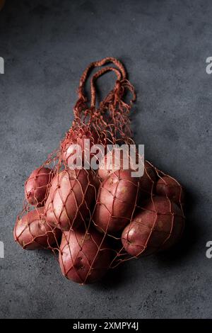 Belles pommes de terre nouvelles roses dans un sac en maille tricoté sur un fond sombre Banque D'Images