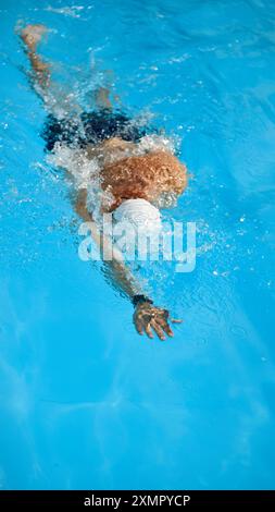 Vue de dessus de l'homme musclé, nageur en bonnet blanc en mouvement, montrant la force pendant la séance d'entraînement nager dans la piscine en plein air. Banque D'Images