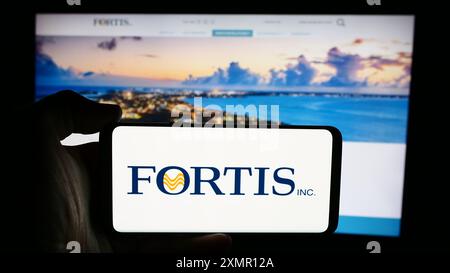 Personne tenant un téléphone cellulaire avec le logo de la compagnie canadienne de services publics d'électricité Fortis Inc. devant la page Web de l'entreprise. Concentrez-vous sur l'affichage du téléphone. Banque D'Images