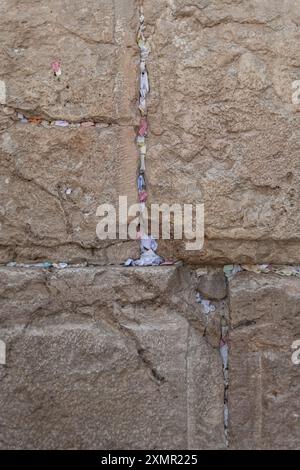 Notes de papier avec bénédictions et prières à l'intérieur des fissures du mur occidental. Le mur occidental, également connu sous le nom de mur des lamentations à l'Ouest et mur d'Al Buraq dans l'Islam, est une destination de pèlerinage pour les croyants juifs. Situé dans la vieille ville de Jérusalem, il fait partie du mur de soutènement du Mont du Temple. Une cloison métallique divise la zone en deux : les hommes à gauche et les femmes à droite. Tout au long de la journée, les croyants juifs visitent le site pour prier, lire les livres sacrés de la Torah et laisser une note de papier à l’intérieur des fissures du mur. Toute la zone est surveillée par des soldats israéliens. Banque D'Images