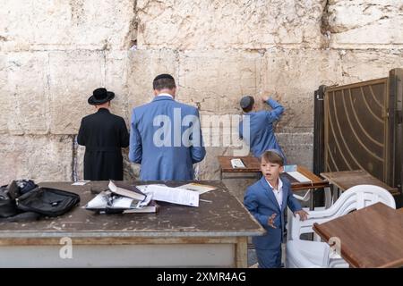 26 juillet 2024, Jérusalem, Israël : des fidèles juifs prient du côté des hommes du mur Occidental, tandis qu'un adolescent insère une note de papier à l'intérieur de la fissure du mur. Le mur occidental, également connu sous le nom de mur des lamentations à l'Ouest et mur d'Al Buraq dans l'Islam, est une destination de pèlerinage pour les croyants juifs. Situé dans la vieille ville de Jérusalem, il fait partie du mur de soutènement du Mont du Temple. Une cloison métallique divise la zone en deux : les hommes à gauche et les femmes à droite. Tout au long de la journée, les croyants juifs visitent le site pour prier, lire les livres sacrés de la Torah et laisser une note de papier à l’intérieur du wa Banque D'Images