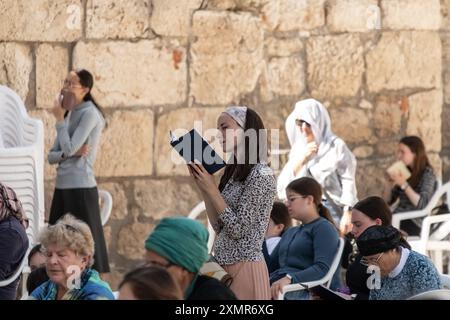 Les adorateurs juifs prient du côté des femmes du mur occidental. Le mur occidental, également connu sous le nom de mur des lamentations à l'Ouest et mur d'Al Buraq dans l'Islam, est une destination de pèlerinage pour les croyants juifs. Situé dans la vieille ville de Jérusalem, il fait partie du mur de soutènement du Mont du Temple. Une cloison métallique divise la zone en deux : les hommes à gauche et les femmes à droite. Tout au long de la journée, les croyants juifs visitent le site pour prier, lire les livres sacrés de la Torah et laisser une note de papier à l'intérieur des fissures du mur. Toute la zone est surveillée par des soldats israéliens. Banque D'Images