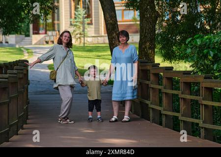 Trois générations de famille, dont une femme âgée, une femme adulte et un enfant, debout sur un pont en bois dans un parc. Portrait extérieur pour le design et Banque D'Images