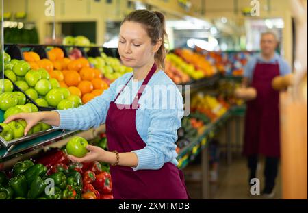 Une vendeuse d'âge moyen met des pommes dans une étaie alimentaire dans une épicerie Banque D'Images