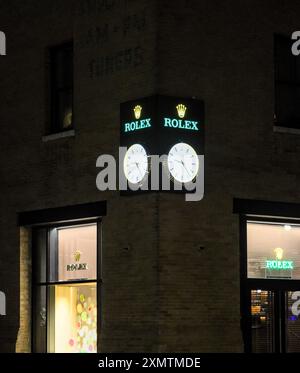 New York, NY - 9 juillet 2024 : logo de fabricant de montres de luxe Rolex avec horloge sur le côté du bâtiment du magasin à Manhattan, New York la nuit après la tombée de la nuit. Banque D'Images