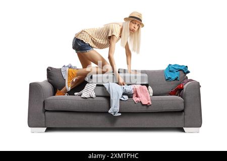 Jeune femme essayant de fermer une valise sur le dessus d'un canapé isolé sur fond blanc Banque D'Images