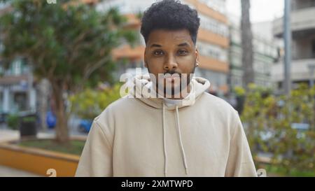 Bel homme noir dans une tenue décontractée posant avec confiance dans un cadre de parc de la ville avec verdure Banque D'Images