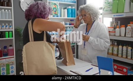 Pharmacienne femme âgée aidant une cliente femme d'âge moyen à un comptoir de pharmacie à l'intérieur Banque D'Images