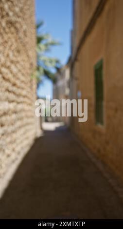 Ruelle défocalisée à majorque, en espagne, présentant des paysages extérieurs flous avec des murs de pierre rustiques sous un ciel bleu éclatant. Banque D'Images