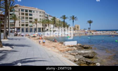 Photo floue d'un front de mer avec des gens profitant de la journée d'été sur une promenade bordée de palmiers et de bâtiments modernes en bord de mer. Banque D'Images