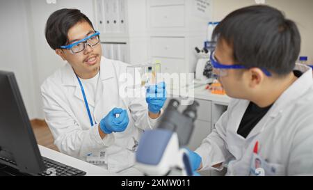 Deux hommes en blouse de laboratoire analysent des échantillons dans un laboratoire scientifique avec des microscopes et des ordinateurs. Banque D'Images