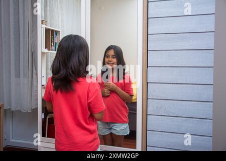 Une fille de l'école primaire chante devant le miroir, en utilisant un peigne comme microphone Banque D'Images