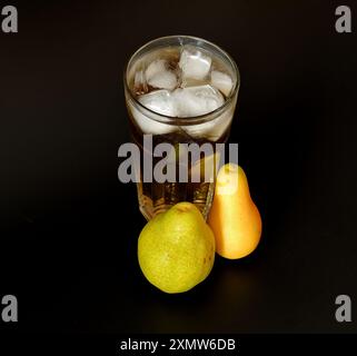 Un mélange de jus de poire de différentes variétés dans un grand verre à facettes avec de la glace sur fond noir, à côté de fruits mûrs. Gros plan. Banque D'Images